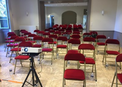 Salle de réunion disposée en théâtre avec des chaises rouges. Conférence